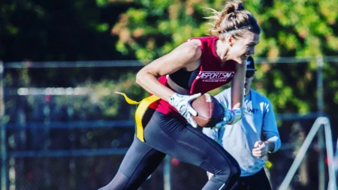 A young woman running with a football during an adult football league in Los Angeles, California.