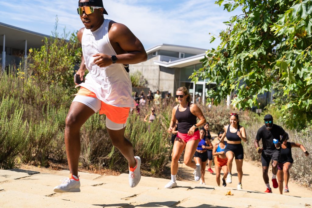 a group of young adults on a jog in a warm area with lots of sunlight and greenery among the active group