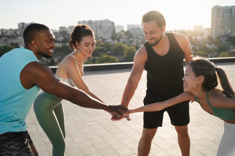 A group of four athletes in workout gear place their hands together in the center for a motivational huddle.