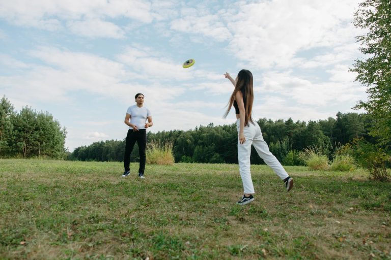 A man and woman play frisbee in a wide, grassy field under a bright, slightly cloudy sky.